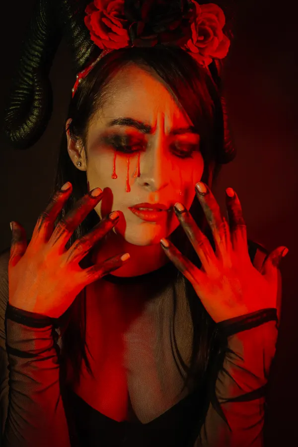A woman with horns and red roses in her hair, painted blood tears, red light on her hands.