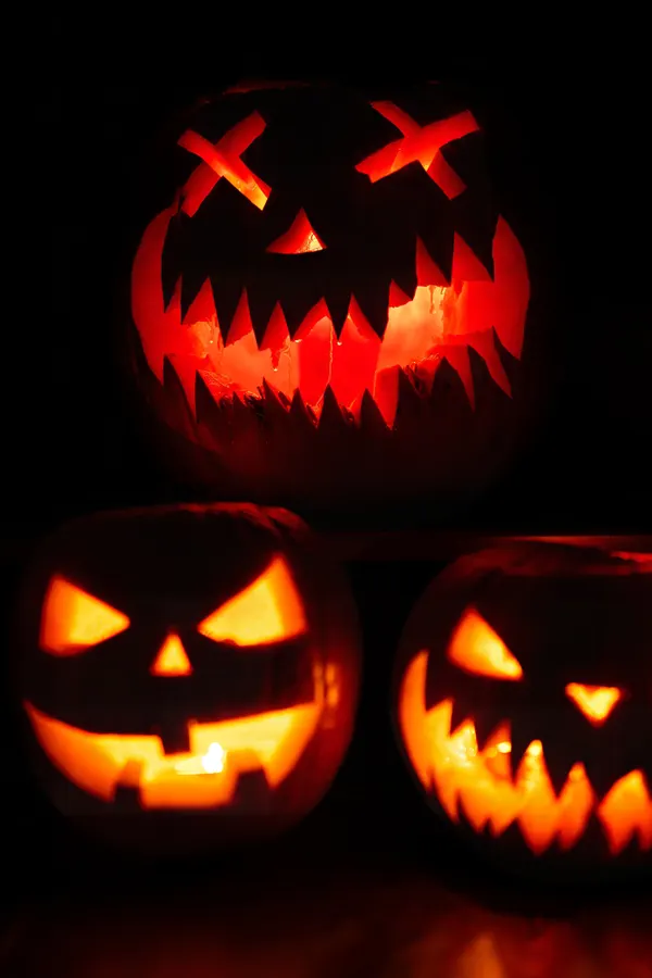 Three carved pumpkins glowing in the dark, one with crossed-out eyes.