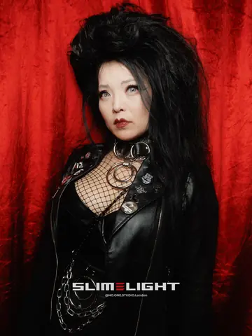 A guest with big black hair and a fishnet top against a red curtain.