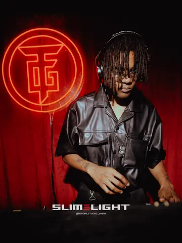 A DJ in a black leather shirt at the decks, a red neon logo on the wall behind.