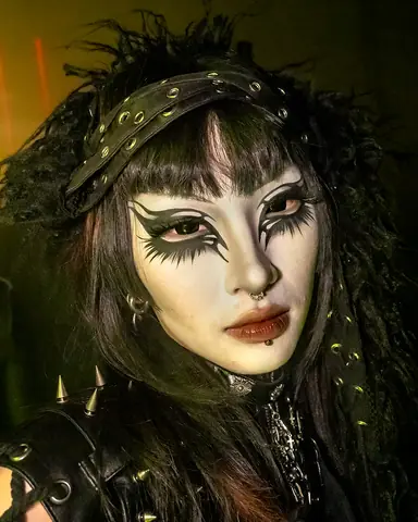 A guest in a studded headband and a feathered collar, with dramatic black eye make-up.